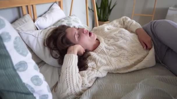 Attractive pretty woman falls asleep in a cozy bed with lots of pillows, looking for a comfortable sleeping position. Hygge - Felvétel, videó