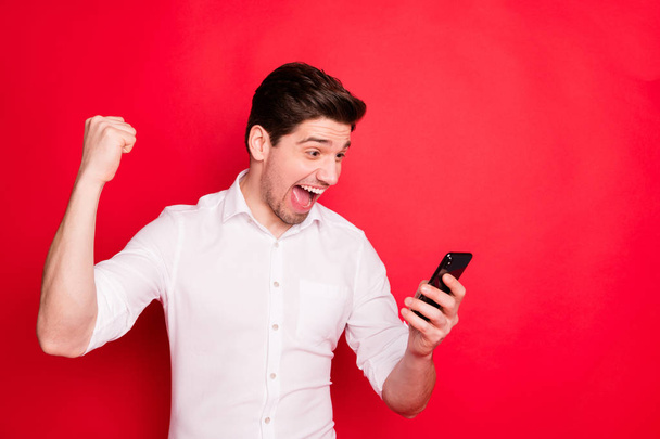 Photo of overjoyed brunet trendy man observing his salary increased on phone while isolated with red background - Foto, Bild