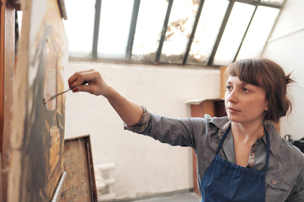 Woman artist paints a picture on canvas. Bright art studio with a large window. Easels and canvases. - Photo, image