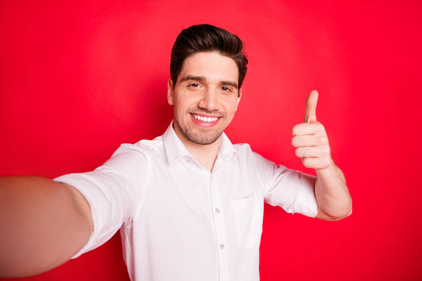 Self portrait of cheerful positive brunet man showing you thumb up sign to recommend something while isolated with red background - Photo, image