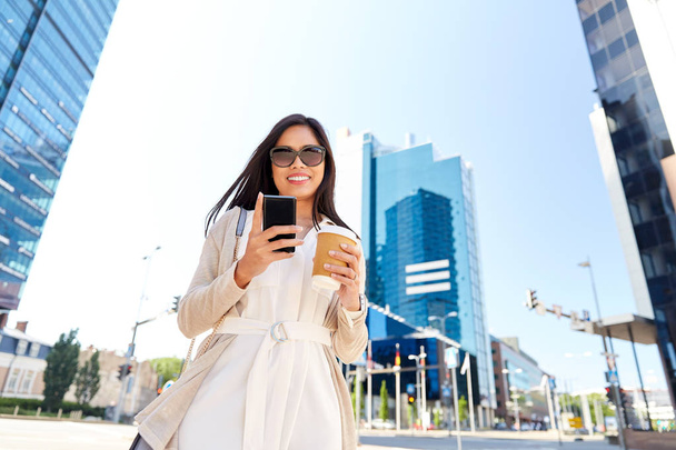 smiling woman with smartphone and coffee in city - Photo, image
