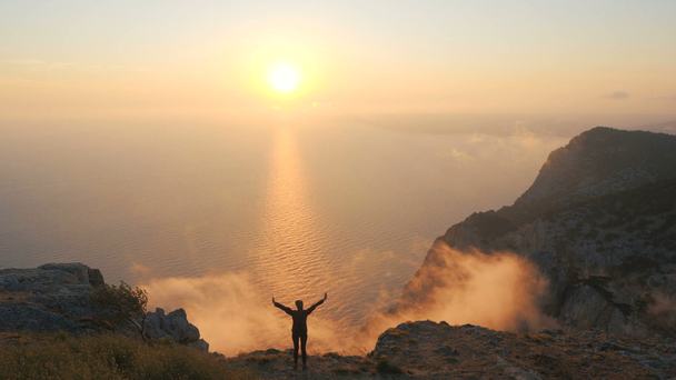シルフエット若い女性の腕は、クリミアの高い山の頂上から海の上に美しい劇的な夕日を観察して伸びた. - 映像、動画