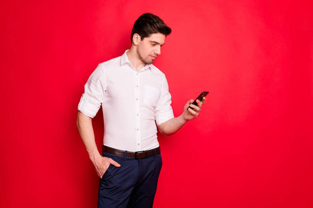 Photo of attractive man staring at telephone in search of something interesting while isolated with red background - Foto, Imagem