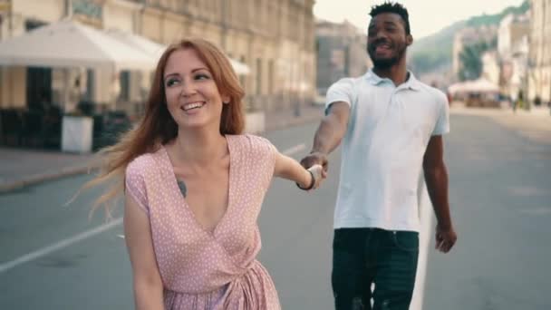 Young happy woman leads her boyfriends hand along city street - Video
