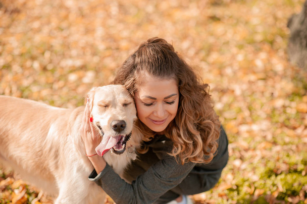 Closeup of curly woman sitting with her dog in autumn leaves outdoors - 写真・画像