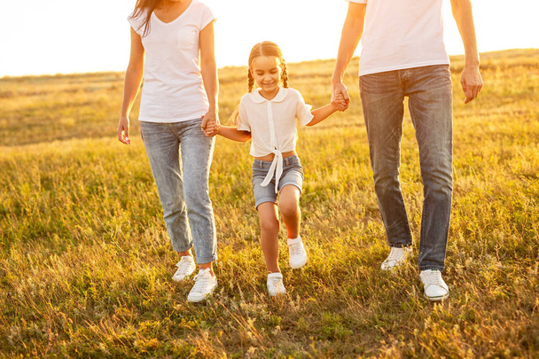 Fröhliche Tochter spaziert mit anonymen Eltern auf Feld - Foto, Bild