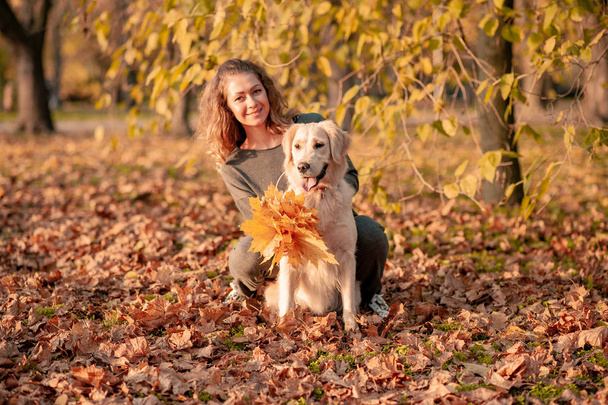 Gros plan de la femme bouclée assise avec son chien dans les feuilles d'automne à l'extérieur
 - Photo, image
