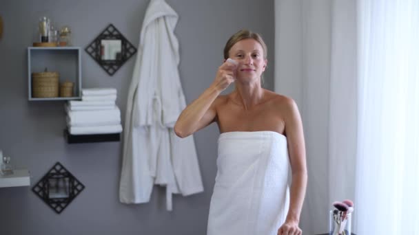 Massaggio viso. Bella donna avvolta in asciugamano dopo la doccia sta ottenendo massaggio viso utilizzando massaggiatore di pietra di giada
 - Filmati, video