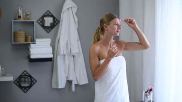 Face massage. Beautiful woman wrapped in towel after shower is getting massage face using jade roller massager - Felvétel, videó