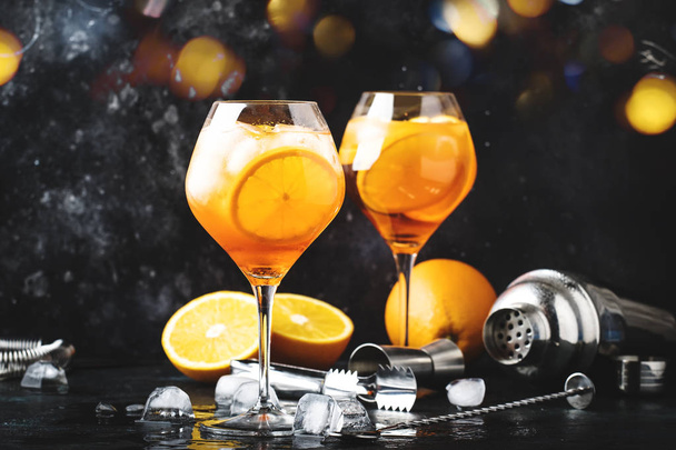 Aperol spritz cocktail in big wine glass with orange and ice, summer alcoholic cold drink, dark bar counter with steel bar tools, copy space - Фото, зображення