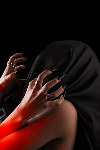 a woman covered with black cloth with a closed face suffers. faceless pain. long black nails on thin female fingers. emotion without facial expressions - Photo, image