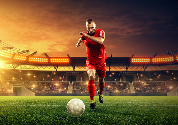 Voetbalspeler in actie op een voetbalstadion. Verlichte nacht veld met verlichting en tribunes. Nacht dramatische hemel - Foto, afbeelding