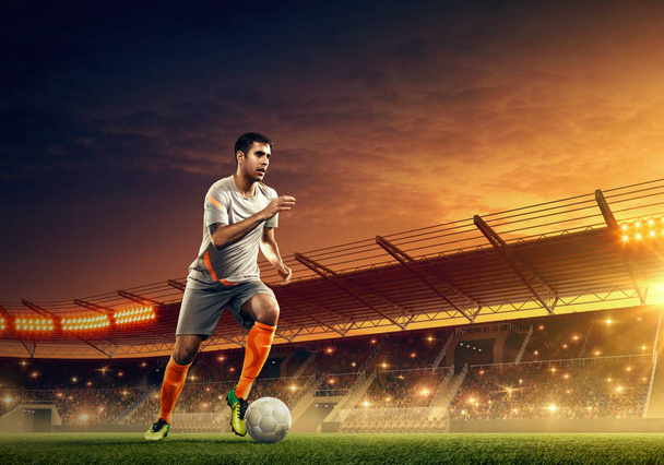 Soccer player in action on a soccer stadium. Floodlit night field with illumination and tribunes. Night dramatic sky - Photo, Image
