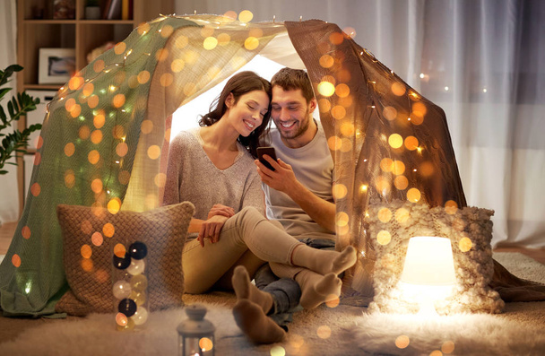 feliz pareja con smartphone en tienda de campaña para niños en casa
 - Foto, Imagen