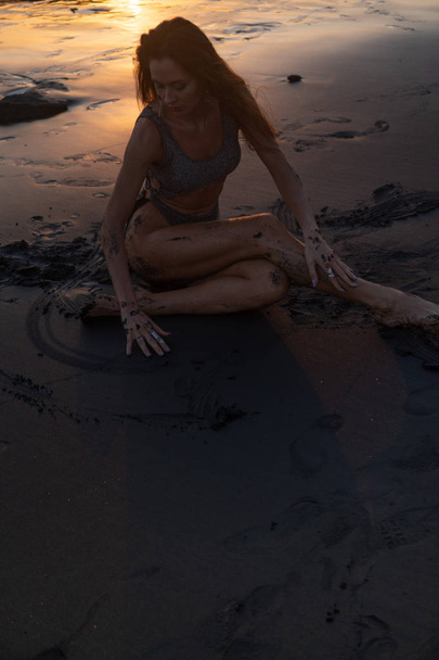 Bella donna sensuale in costume da bagno scintillante in posa presso la spiaggia di sabbia nera durante sorprendente tramonto dorato
 - Foto, immagini