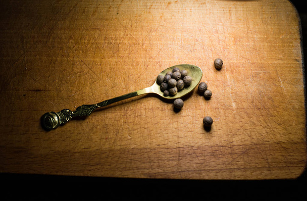 Pimenta preta em uma colher em uma tábua de madeira
 - Foto, Imagem
