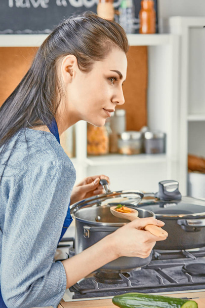Bella ragazza sta assaggiando il cibo e sorridendo mentre cucina in kit
 - Foto, immagini