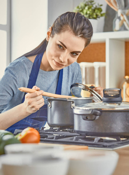 Beautiful girl is tasting food and smiling while cooking in kit - Foto, Imagen