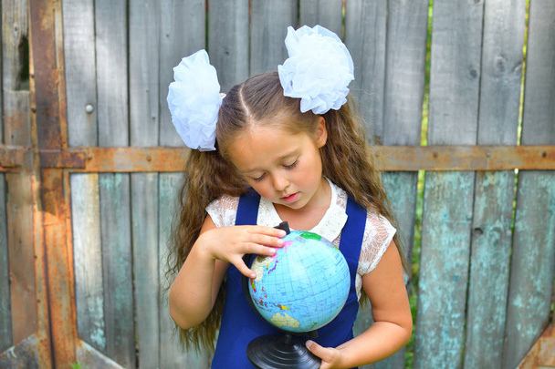  Porträt einer schönen jungen Schülerin, die durch ein Vergrößerungsglas auf den Globus auf dem Hintergrund eines alten Holzzauns blickt. - Foto, Bild