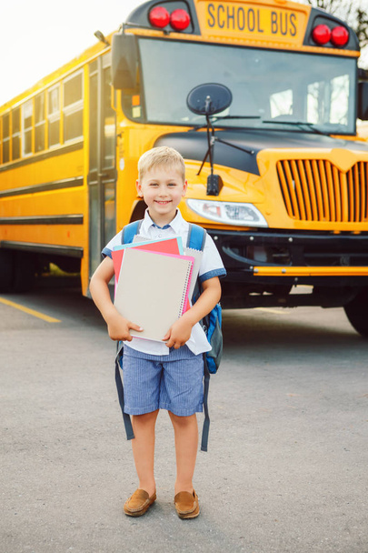 lustige süße fröhliche kaukasische Junge Student Kind mit Rucksack und exrecise Bücher in der Nähe gelben Bus am 1. September Tag. Bildung und zurück zum Schulkonzept. Schüler lern- und lernbereit.  - Foto, Bild