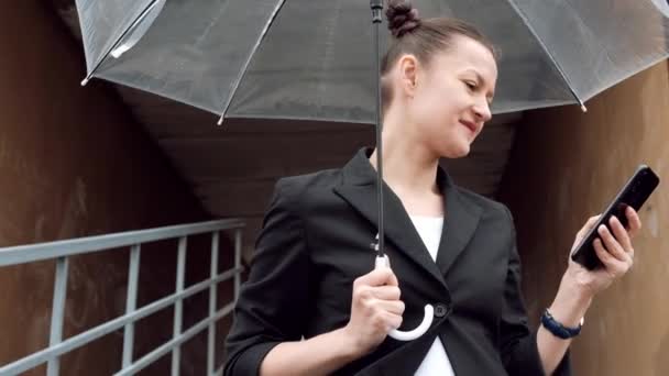 Young attractive woman in black jacket and blue jeans posing outdoor against background of building. - Materiał filmowy, wideo