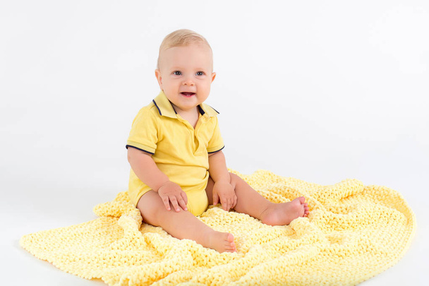 Hymyilevä lapsi poika pehmeällä keltaisella peitolla valkoisella taustalla
 - Valokuva, kuva
