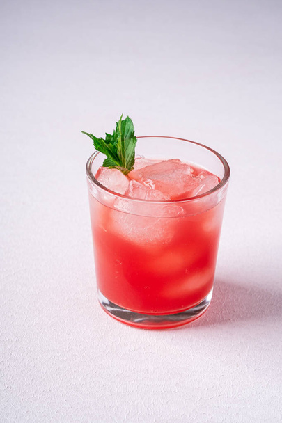 Fresh cold watermelon juice with ice cubes and green mint leaf in glass drink on white background, copy space, angle view - Foto, afbeelding