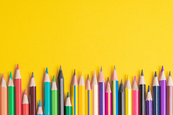 Many sharpened colored pencils laid out on a yellow background.  - 写真・画像