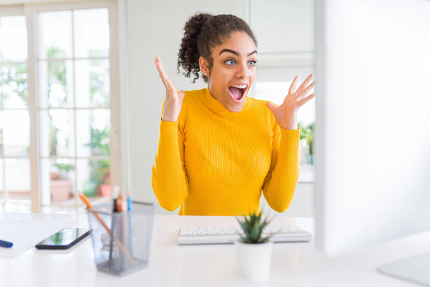 Fiatal afro-amerikai lány dolgozik a számítógépes nagyon boldog és izgatott, győztes kifejezés ünneplő győzelme sikoltozik a nagy mosoly, és emelt kezek - Fotó, kép
