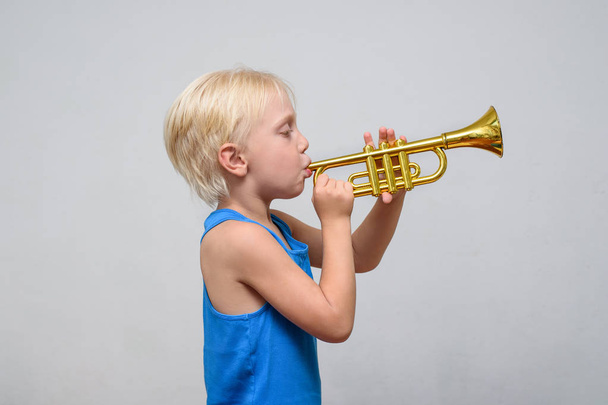 Little cute blond boy playing toy trumpet on light background - Foto, afbeelding