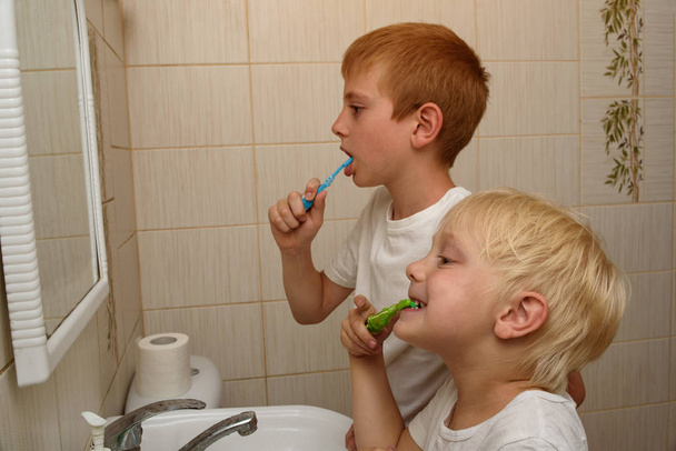 Két fiú kefe foguk előtt egy tükör a fürdőszobában. Reggeli higiénia - Fotó, kép