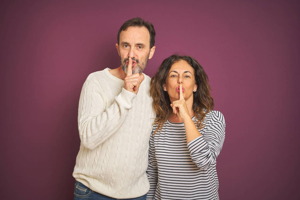 Красива пара середнього віку в зимовому светрі над ізольованим фіолетовим тлом з проханням бути тихим пальцем на губах. Тиша і таємна концепція
. - Фото, зображення
