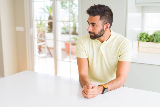 Camiseta amarilla casual de hombre hispano guapo en casa mirando al costado, pose de perfil relajado con cara natural con sonrisa confiada
. - Foto, imagen