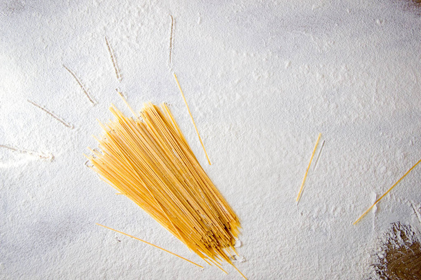 Uncooked pasta spaghetti on floured white background. Hand drawn sun beams on table, simple cartoon style - Photo, image
