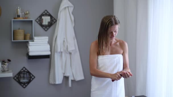 Hair care concept. Beautiful woman wrapped in towel after shower is applying coconut oil her wet hair - Felvétel, videó
