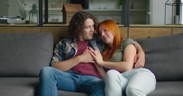 Νεαρό ζευγάρι σε ρομαντική διάθεση κάθεται στον καναπέ στο σπίτι - Πλάνα, βίντεο