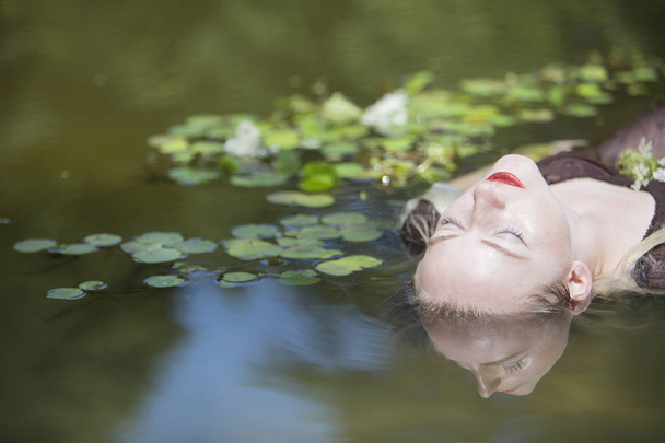 πορτρέτο με αντανάκλαση μιας όμορφης νεαρής γυναίκας σε μια λιμνούλα με κρίνα νερού - Φωτογραφία, εικόνα