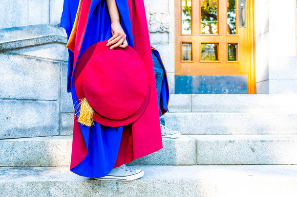 Кандидат (докторський) випускник у регалії, тримаючи капелюх Тюдора, сидячи на університетських сходинках, з взуттям для кросівок. Червоно-синя сукня, золота тасьма, що показує
. - Фото, зображення
