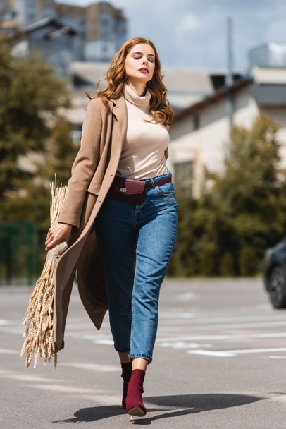 atrakcyjna kobieta z zamkniętymi oczami w płaszczu spacerów i trzymania kolców - Zdjęcie, obraz