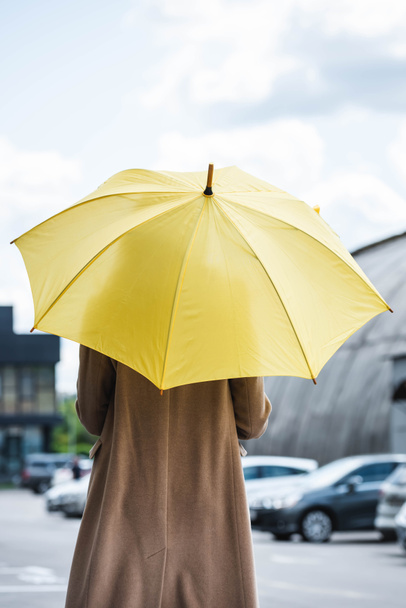 back view of woman in coat holding yellow umbrella  - Foto, afbeelding