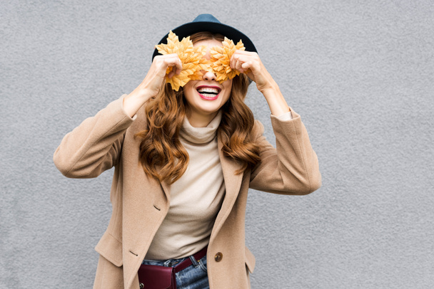 woman in blue hat smiling and holding yellow leaves  - Photo, Image