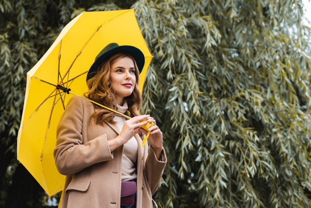 vonzó nő, kék kalapot néz el, és a gazdaság sárga esernyő  - Fotó, kép