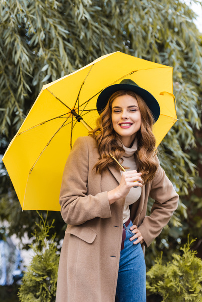 attractive woman in blue hat looking at camera and holding yellow umbrella  - Foto, immagini