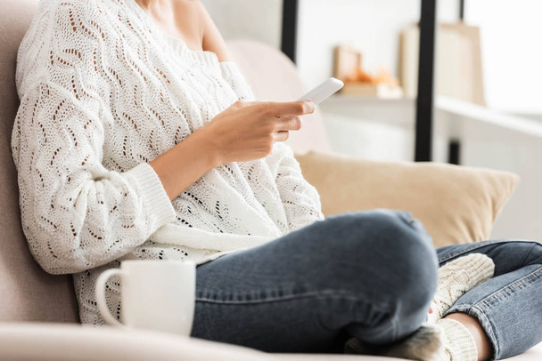 cropped view of woman in white sweater and jeans using smartphone  - Zdjęcie, obraz