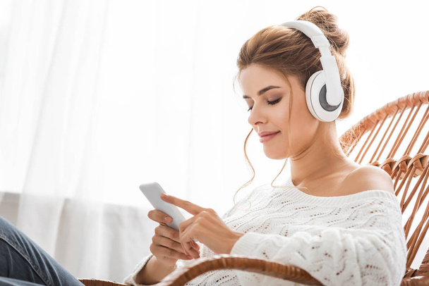 attraktive Frau im weißen Pullover, die Musik hört und das Smartphone benutzt  - Foto, Bild