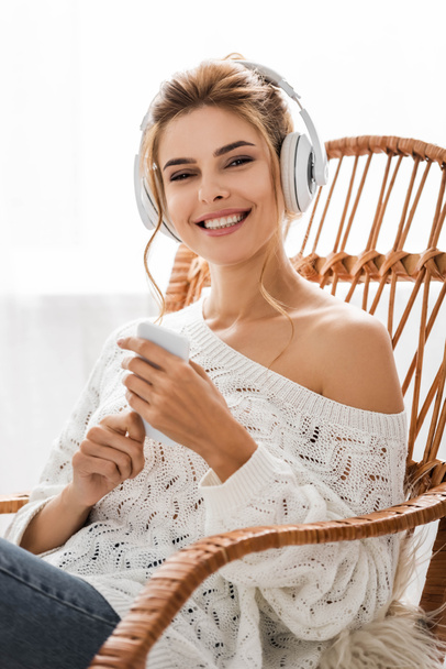 attractive woman in white sweater listening music and holding smartphone  - Fotografie, Obrázek