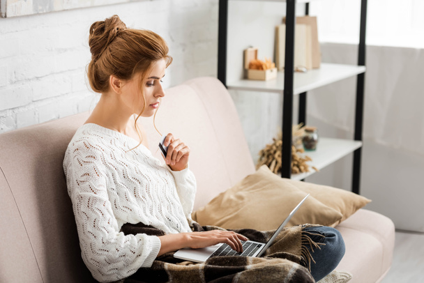 attractive woman in white sweater holding credit and laptop - Foto, imagen