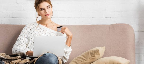 panoramic shot of attractive woman in white sweater holding credit and laptop - Photo, Image