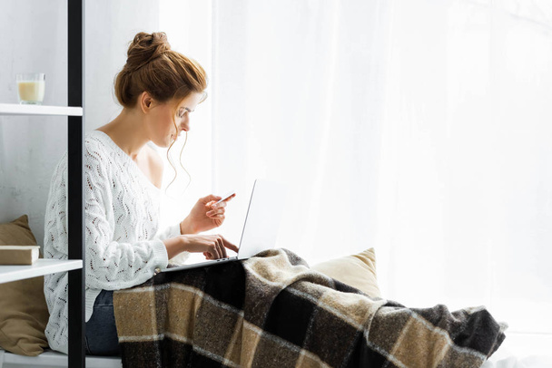 attractive woman in white sweater holding credit and laptop - Φωτογραφία, εικόνα