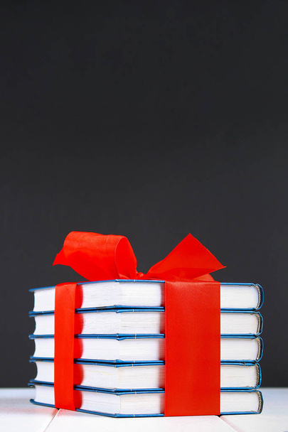 Ένας σωρός από βιβλία δεμένα με μια κόκκινη κορδέλα σε ένα λευκό ξύλινο τραπέζι. - Φωτογραφία, εικόνα